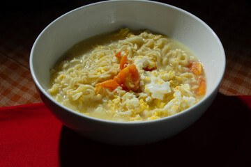 mixed noodle soup with egg and tomatoes in a white bowl on a table mat