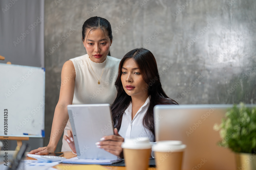 Wall mural two gorgeous asian businesswomen are focused on working on a business project together in the office