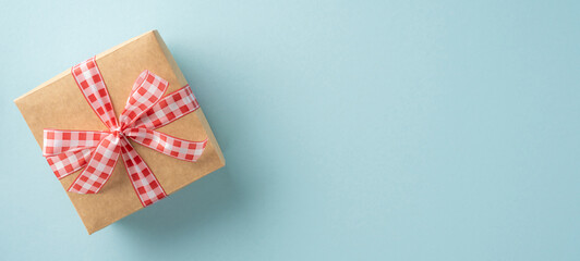 A brown gift box wrapped in red checkered ribbon rests on a light blue background conveying simplicity and elegance