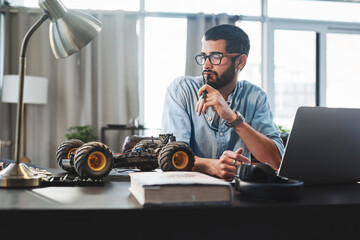 Laptop, robotics and thinking with engineer man in home office for invention or remote work. Car, idea and model with male person on computer in apartment for problem solving or vehicle design