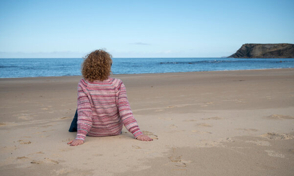 Woman relaxing on a sandy beach with a scenic view of cliffs and sea