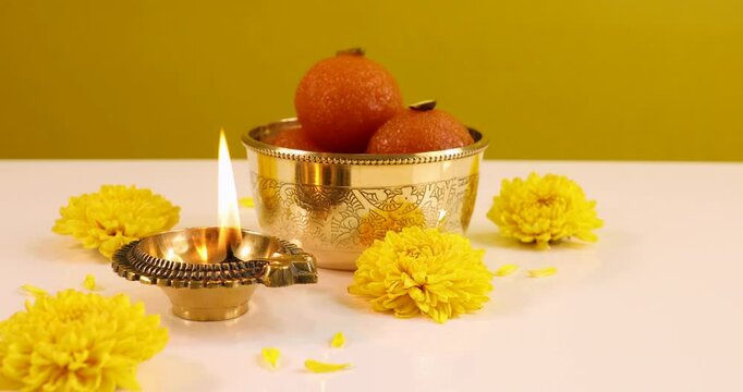 Close-up view of beautiful burning Oil lamp Diya during Diwali Festival decorated with Indian sweet laddu, yellow flowers, isolated over yellow background. Festival of lights.