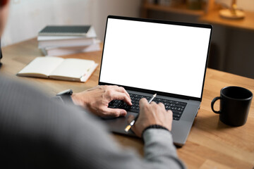 Close-up image of a man working on laptop computer at a table, typing on the laptop keyboard. the laptop with a white screen mockup