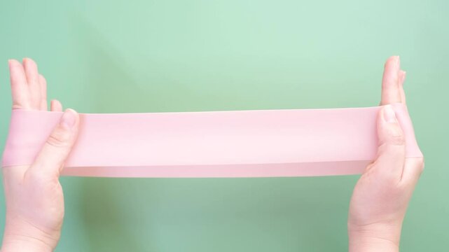 Hands stretching fitness elastic band on green background close-up.