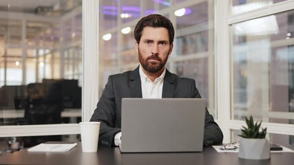 Businessman works on his laptop in the office. He is serious and focused on his work. The modern office is bright and airy.