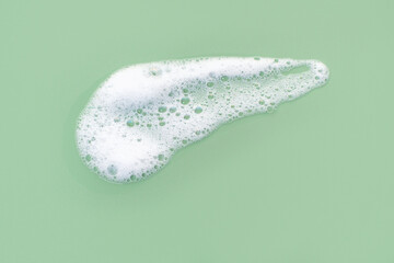 Smear of facial cleansing foam on green background close-up.
