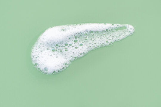 Smear of facial cleansing foam on green background close-up.