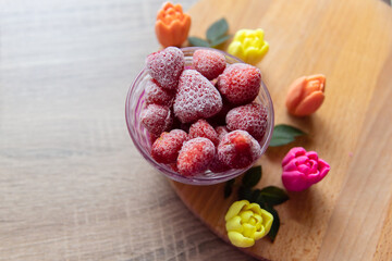 Bowl of Frozen Strawberries on Wooden Surface with Colorful Decorative Flowers