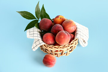 Wicker bowl with sweet peaches and leaves on blue background