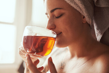 Woman, relax and drinking with tea by window for morning routine, hygiene or cleanse in bathroom at home spa. Young, female person or smile with beverage for calm, detox or peaceful day at house