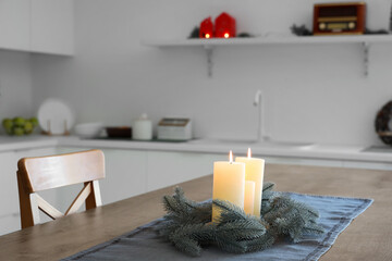 Burning candles and Christmas wreath on wooden table in kitchen, closeup