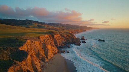 Obraz premium Aerial view of a dramatic coastline with cliffs, a sandy beach, and the ocean in the distance. The sky is filled with beautiful clouds, and the sun is setting in the background.