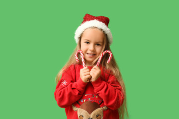 Cute little girl in elf costume with candy canes on green background