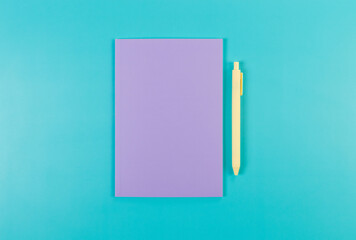 Top view of purple notebook, yellow pen on blue background. School, office wallpaper. Flat lay, copy space.