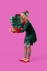 Beautiful young woman dressed as elf with Christmas gifts on purple background