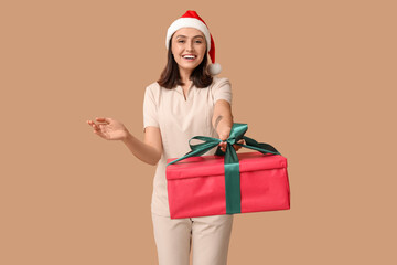 Beautiful female massage therapist in Santa hat with gift box on brown background