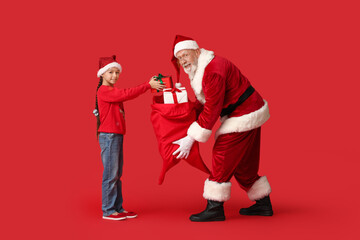 Happy cute little girl and Santa Claus holding bag with gift boxes on red background