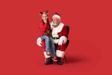 Santa Claus and cute little girl sitting on armchair against red background