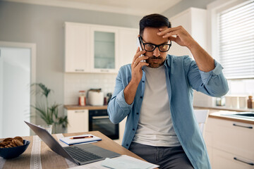 Distraught man making  phone call while working on laptop at home.