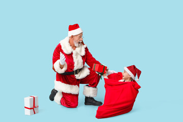 Santa Claus and cute little girl with gift boxes sitting in bag on blue background