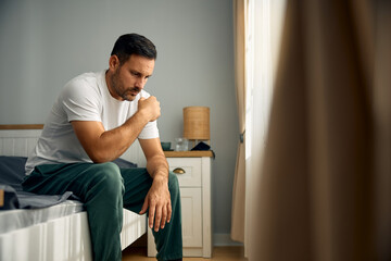 Mid adult man coping with depression while sitting alone in morning in bedroom.