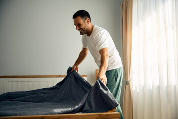 Happy man making his bed after waking up in  morning.