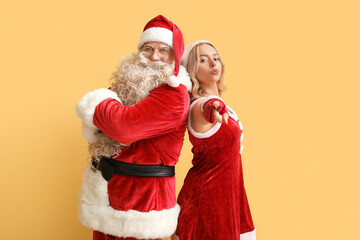 People dressed as Santa Claus pointing at viewer on yellow background