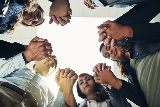 Low angle, praying and holding hands with business people in office for support, community and team building. Joint venture, worship and sympathy with group of employees for merger, faith and trust