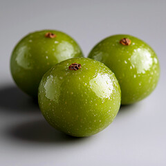 Obraz premium Three shiny green fruits arranged closely on a gray surface.