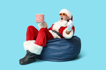 Shocked Santa Claus in 3D glasses with bucket of tasty popcorn on blue background