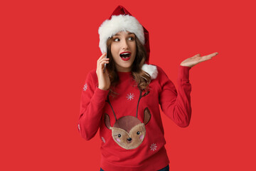 Young woman in Santa hat talking by mobile phone on red background
