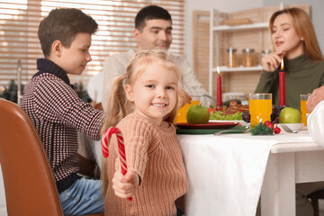 Little girl with candy cane having family dinner at home on Christmas eve