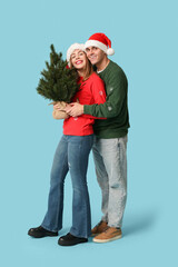 Happy young couple in Santa hats with Christmas tree on blue background