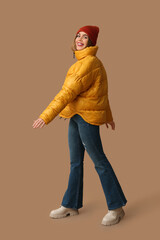Fototapeta premium Beautiful young happy woman in warm winter clothes on brown background