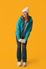 Beautiful young happy woman in warm winter clothes on yellow background