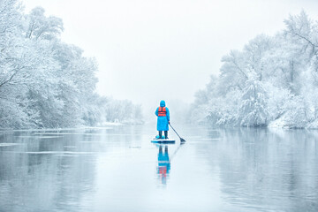 a man on a supboard in the winter on a river in the woods