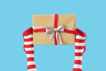 Fototapeta premium Female legs in Christmas stockings and high heeled shoes with gift box on color background