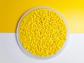 Yellow masterbatch granules in a cup on a yellow and white background, a color pigment carrier...
