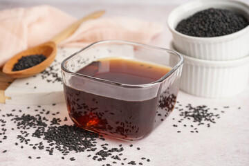 Bowl of oil with sesame seeds on white background
