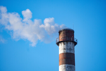 Industrial chimney emitting smoke. Red and white chimney. Environmental pollution.