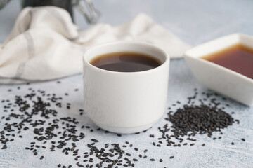 Cup of oil with sesame seeds on white grunge background