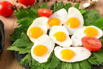 Plate with fried quail eggs, parsley and tomatoes on wooden background