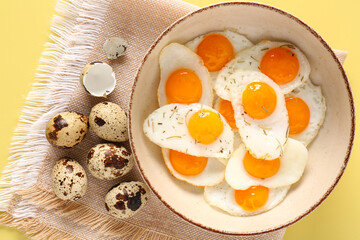 Bowl with fried quail eggs on yellow background