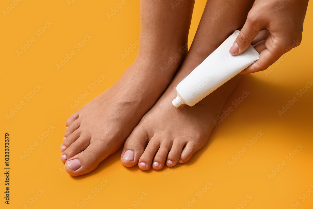 Wall mural Young woman with beautiful pedicure applying cosmetic product on yellow background