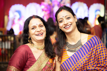 Two joyful Indian women laughing and posing at a Durga Puja pandal during the Navratri festival, celebrating culture and togetherness.