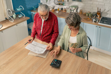 in bright kitchen an elderly cute couple at the table count their expenses monthly payment summing up the results of the year utilities count monthly survival count money