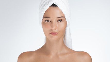 A calm woman with a towel wrapped around her head gazes into the camera, exuding peace during her skincare routine. Perfect for illustrating themes of beauty, self-care, and the soothing effects of a