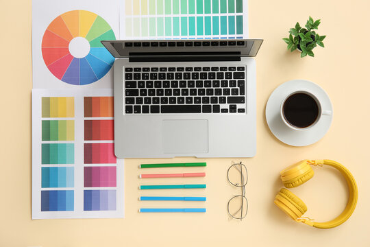 Workplace of graphic designer with laptop, coffee and color charts on yellow background