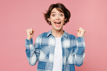 Young happy woman she wear blue shirt white t-shirt casual clothes doing winner gesture celebrate clenching fists say yes isolated on plain pastel light background studio portrait. Lifestyle concept.