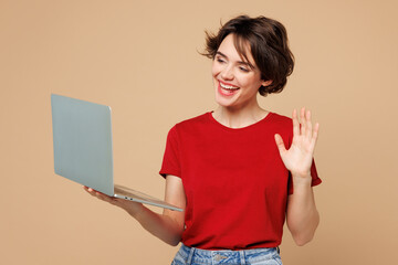 Young smiling happy IT woman wears red t-shirt casual clothes hold use work on laptop pc computer...